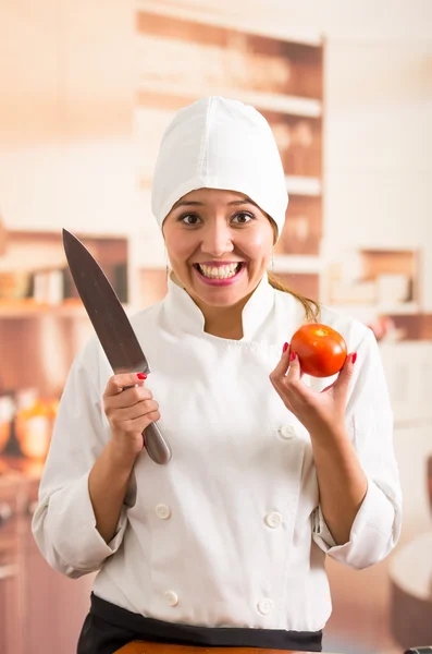 Mujer chef sosteniendo gran cuchillo de metal y tomate mientras sonríe a la cámara —  Fotos de Stock