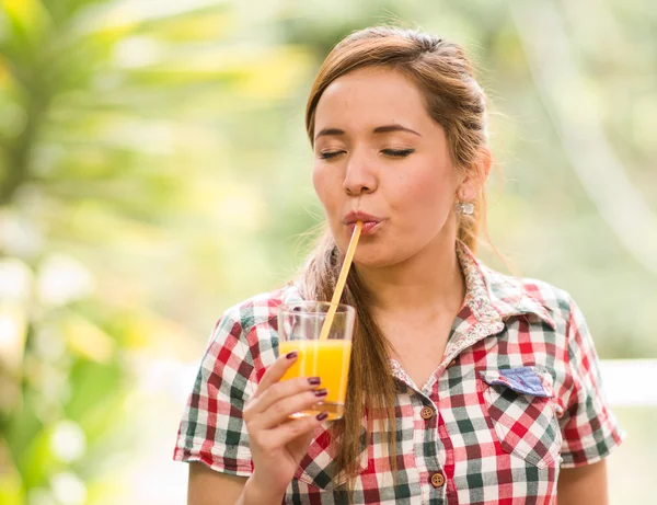 Giovane donna in camicia modello quadrato godendo di un succo giallo con gli occhi chiusi, ambiente giardino — Foto Stock