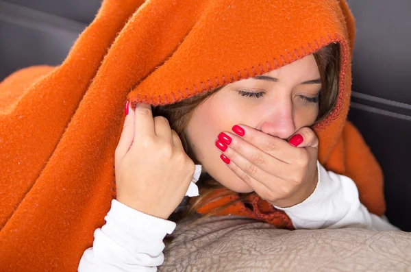 Brunette lying down under orange blanket and covering her mouth using hand, sick with flu concept — Stock Photo, Image