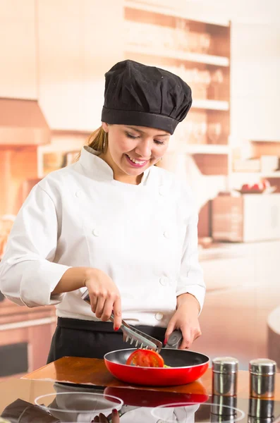 Mujer chef con traje de cocina completo de pie freír verduras en sartén roja —  Fotos de Stock