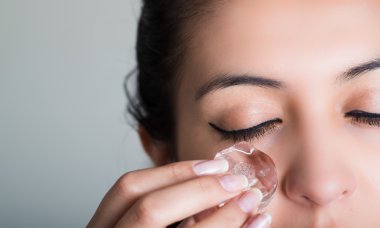 Güzel esmer modeli sürtünme Ice cube yanak göz, gri arka plan altında karşı