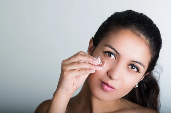 Hermosa modelo morena inclinada cabeza a un lado y frotando el cubo de hielo contra la mejilla debajo del ojo — Foto de Stock