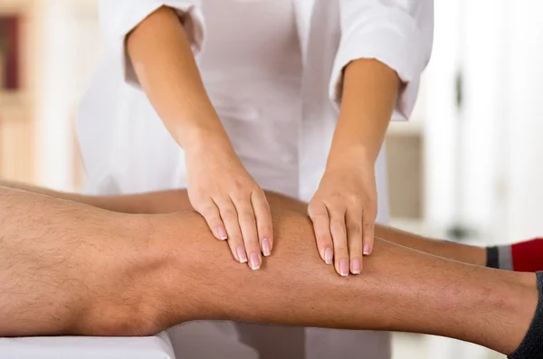 Closeup female physio therapist hands working on male patients legs, blurry clinic background — Stock Photo, Image