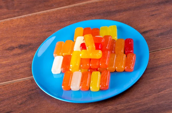 Colorful rectangular hard candy placed on blue plate with wooden surface background — Stock Photo, Image