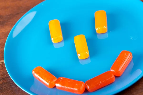 Doces duros retangulares coloridos colocados como rosto sorridente na placa azul com fundo de superfície de madeira — Fotografia de Stock