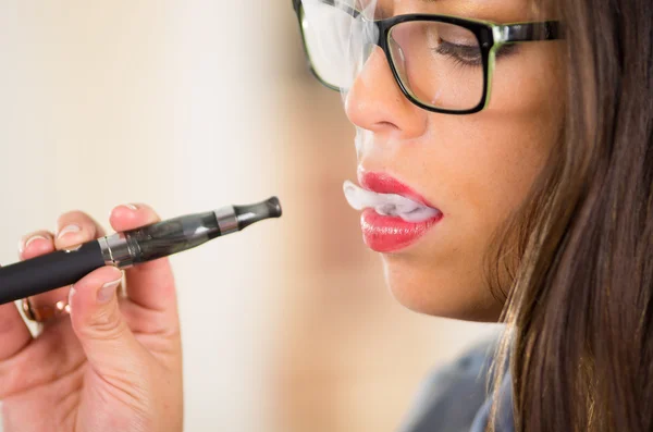 Närbild brunett bär glasögon och ljusa läppstift vaping, rökning e-cigarett med rök synlig — Stockfoto