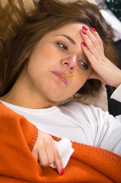 Brunette lying down under orange blanket, thermometer in mouth, sick with flu concept — Stock Photo, Image