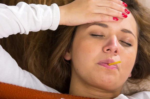 Brunette lying down under orange blanket, thermometer in mouth, sick with flu concept — Stock Photo, Image