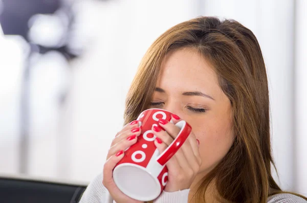 Bruna malata con l'influenza seduta sul divano che beve dalla tazza rossa — Foto Stock