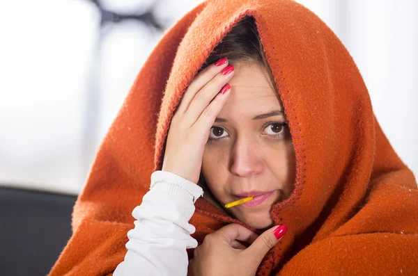 Brunette zitten onder oranje deken, thermometer in de mond, ziek met griep concept — Stockfoto