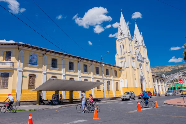 QUITO, ECUADOR - MARZO 23, 2015: Iglesia grande e imponente cubierta por un gran cielo. Beige y amarillo dominaron la arquitectura. Gente unificada cruzando con bicicletas — Foto de Stock