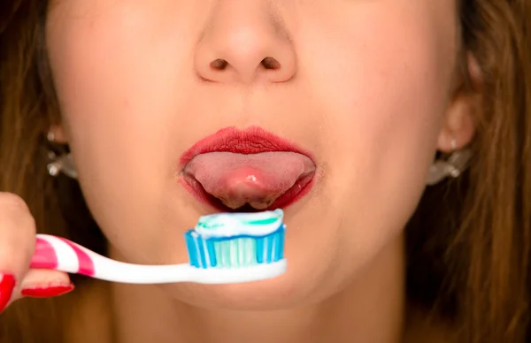 Primer plano las mujeres jóvenes abren la boca con la lengua que sobresale y cepillo de dientes en frente — Foto de Stock