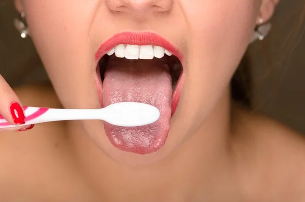 Closeup young womans mouth with tongue sticking out and using toothbrush — Stock Photo, Image