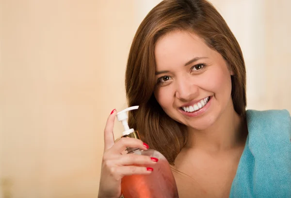 Jonge vrouw houden oranje crème fles en lacht om de camera met blauwe kleding opknoping over de schouder — Stockfoto