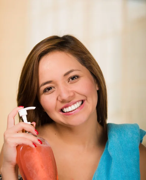 オレンジ クリームのボトルを押しながら肩に青い服吊りとカメラに笑顔の若い女性 — ストック写真