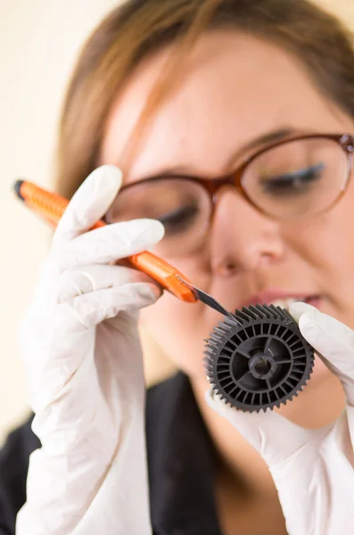 Wanita muda mengenakan kemeja hitam memegang bagian toner dan melihat lebih dekat ke dalamnya saat melakukan pemeliharaan, ekspresi wajah terkonsentrasi — Stok Foto