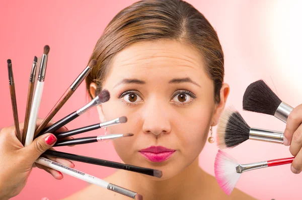 Cabeza joven mujer bastante hispana morena con lápiz labial rojo sosteniendo la selección de pinceles de maquillaje, fondo rosa — Foto de Stock