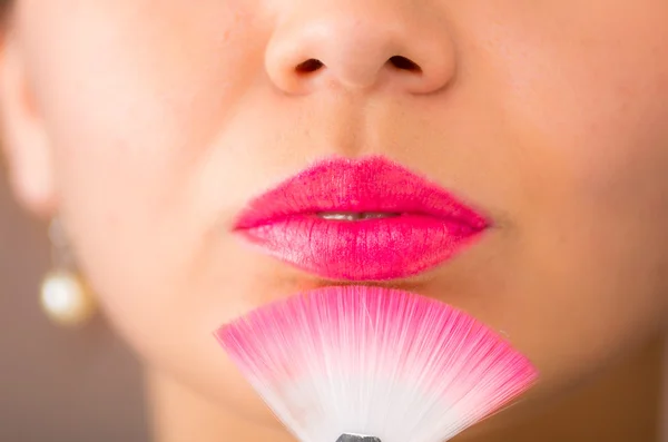 Primer plano de la cabeza joven mujer bastante hispana con lápiz labial rosa sosteniendo cepillo de maquillaje bajo la boca cerrada —  Fotos de Stock