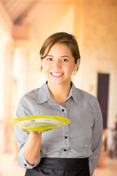 Giovane cameriera bruna indossa uniforme con sorriso amichevole, tenendo il vassoio con una mano, in posa felicemente per la fotocamera — Foto Stock