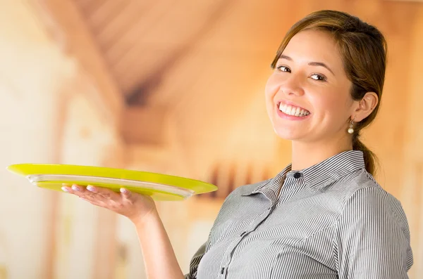 Jovem garçonete morena vestindo uniforme com sorriso amigável, segurando a bandeja usando uma mão, posando feliz para a câmera — Fotografia de Stock