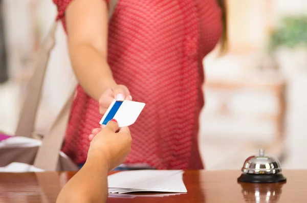 Closeup customer guest and hotel receptionist interacting at front desk, bell sitting on table, exchanging room key — Stock Photo, Image