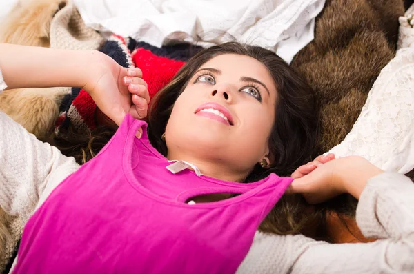 Brunette vrouw liggend op stapel kleren glimlachend poseren natuurlijk winkelen mode concept — Stockfoto