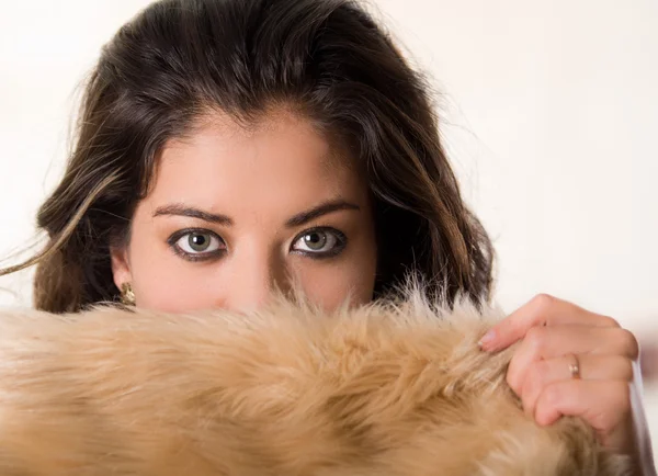 Cabeza morena atractiva frente a la cámara que cubre la mitad de su cara con ropa de piel marrón, fondo de estudio blanco — Foto de Stock