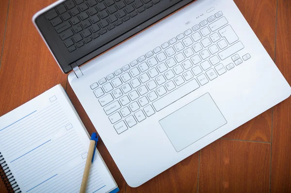 Laptop bianco visto dall'alto seduto su una superficie di legno con blocco note e penna accanto ad esso — Foto Stock