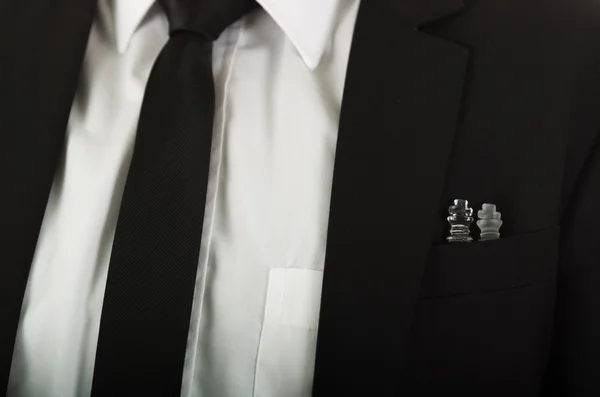 Closeup black suit jacket chest pocket with glass chess pieces sitting inside, white shirt and tie visible — Stock Photo, Image