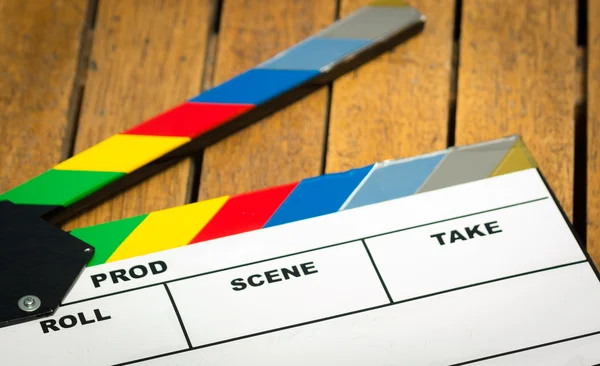 Colorful movie clapboard lying on wooden surface as seen from above — Stock Photo, Image