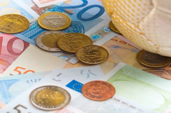 Voetbal, zittend op de verspreiding van de euro geld biljetten en munten, wedden concept — Stockfoto