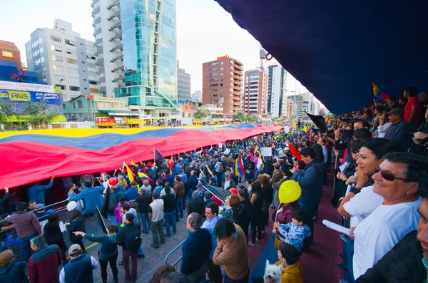 Quito, Equador - 7 de abril de 2016: Grupo de pessoas exibindo uma bandeira equatoriana muito grande, sinais de protesto e jornalistas durante protestos contra o governo na Avenida Shyris . — Fotografia de Stock