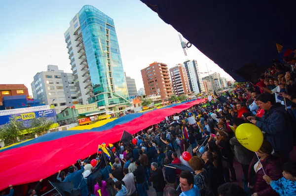 Quito, Equador - 7 de abril de 2016: Grupo de pessoas exibindo uma bandeira equatoriana muito grande, sinais de protesto e jornalistas durante protestos contra o governo na Avenida Shyris . — Fotografia de Stock