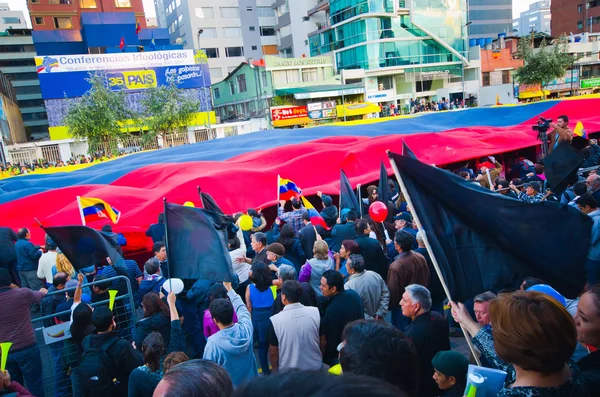 Quito, Ecuador - 7 de abril de 2016: Grupo de personas mostrando una gran bandera ecuatoriana, pancartas de protesta y periodistas durante protestas contra el gobierno en la Avenida Shyris . — Foto de Stock