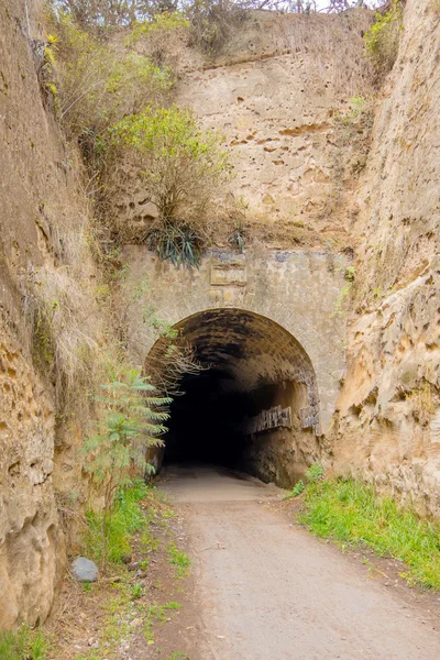 Βαθύ και σκοτεινό σπήλαιο στη μέση του δρόμου ποδηλάτες, δέντρα και Χλόη γύρω από σε μια ωραία μέρα για: Κίτο — Φωτογραφία Αρχείου