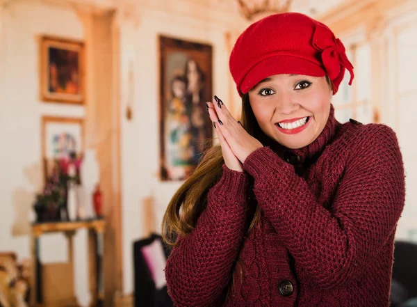 Bella giovane donna bruna vestita con maglione rosso e beenie, che si incrociano le mani, sorridendo come se fosse fredda — Foto Stock
