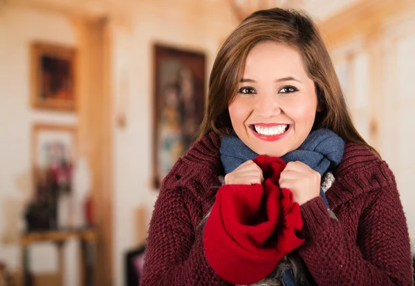 Bella giovane donna bruna che indossa maglione rosso tenendo beenie tra le mani contro la bocca, congelamento concetto freddo — Foto Stock