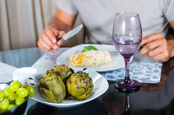 Apparecchiatura di classe tavola da pranzo, carciofi cotti seduti in mezzo, braccia mans visibile tenendo posate accanto al piatto bianco di crepe servire — Foto Stock