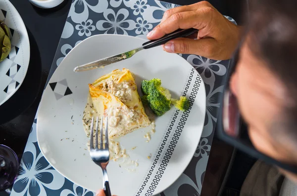 Crepe ricoperto di salsa bianca sdraiato sul piatto con pezzi di broccoli, l'uomo mangia come visto dall'alto, apparecchiare la tavola di classe — Foto Stock