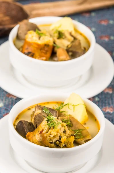 Classy serving of potato soup with meat and vegatables, served in white bowls sitting on table, blue tablecloth, cozy restaurant background — Stock Photo, Image