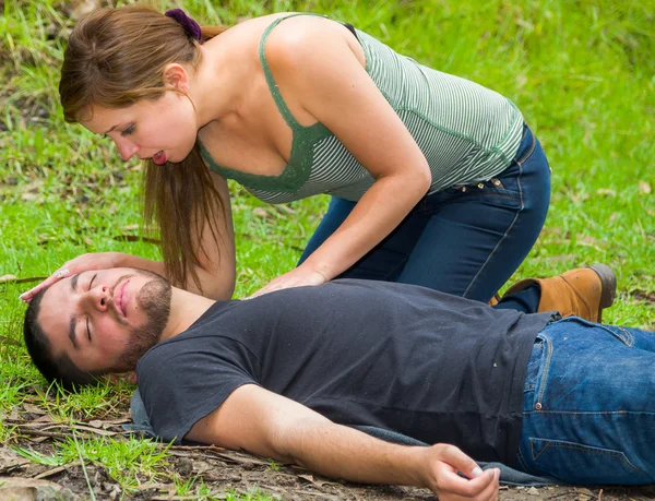 Young man lying down with medical emergency, young woman sitting by his side performing light treatment, outdoors environment — Stock Photo, Image