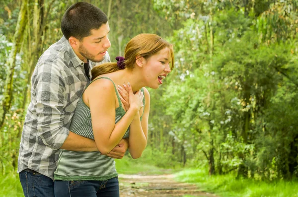 Young woman choking with man standing behind performing heimlich maneuver, park environment and casual clothes — Stock Photo, Image