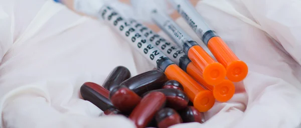 Closeup syringes and pill capsules lying in small pile on white fabric — Stock Photo, Image