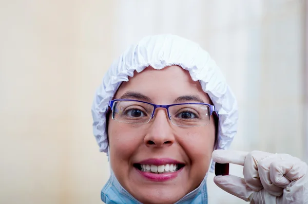 Closeup headshot female nurse wearing bouffant cap and glasses holding up two pill capsules for camera smiling — Stock Photo, Image