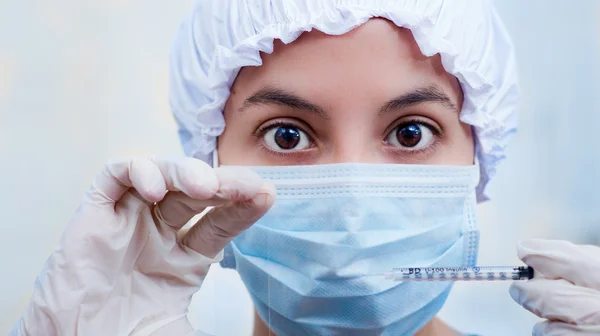 Closeup headshot nurse wearing bouffant cap and facial mask holding up syringe needle for camera — Stock Photo, Image