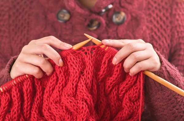 Nahaufnahme Frauenhände mit hölzernen Stricknadeln, die an rotem Schal arbeiten — Stockfoto