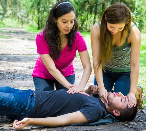 Ung man ligger ned med medicinsk nödsituation, två unga kvinnor utför första hjälpen, utomhus miljö — Stockfoto