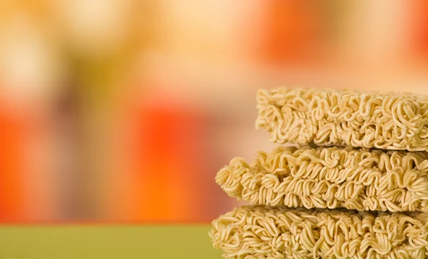 Noodles square blocks stacked on top of each other, green surface and blurry background — Stock Photo, Image