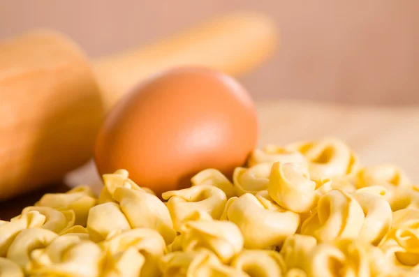 Closeup tortellinis empilhados ao lado de um ovo e desfocado rolando fundo pin — Fotografia de Stock