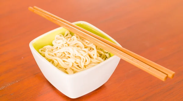Elegant presentation of cooked noodles inside small square bowl sitting on wooden surface, sticks lying across top — Stock Photo, Image